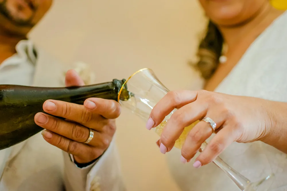A photographed close-up of hands pouring champagne into a glass at a wedding.