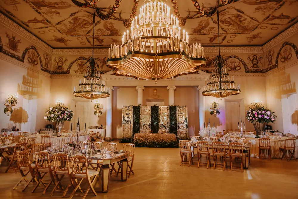 A photographed reception room with chandeliers, flowers and set dining tables.